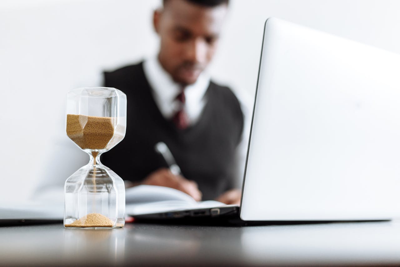 expertise-01 Businessman at desk with hourglass indicating time management and daily work routine.